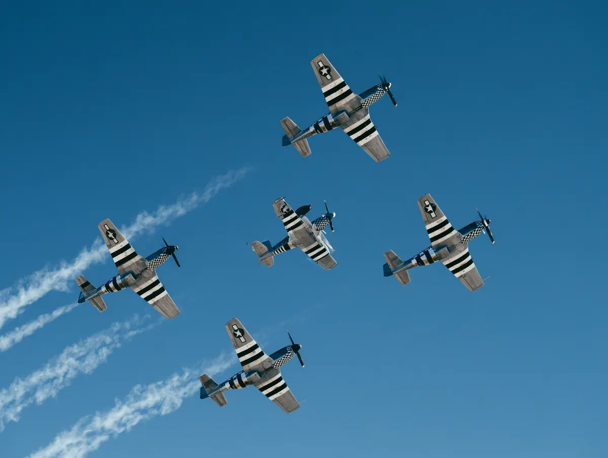 A formation of five P-51 Mustangs with invasion stripes seen from directly below
